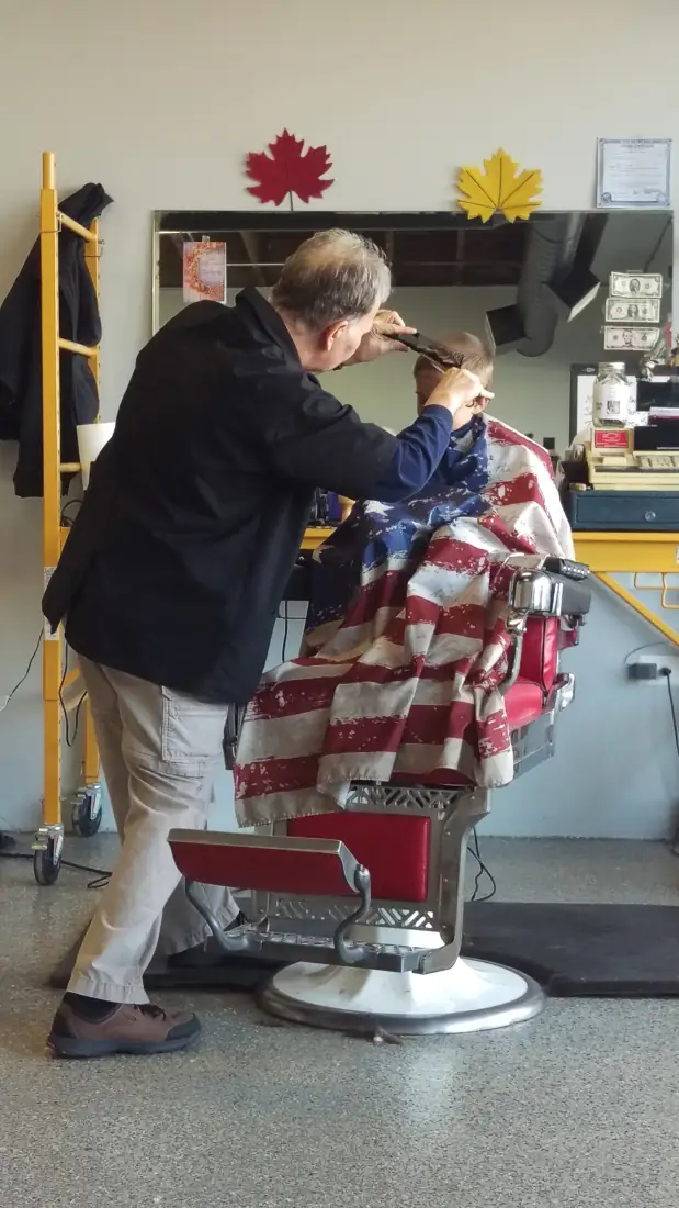 Bob cutting a young boy’s hair under a flag cape